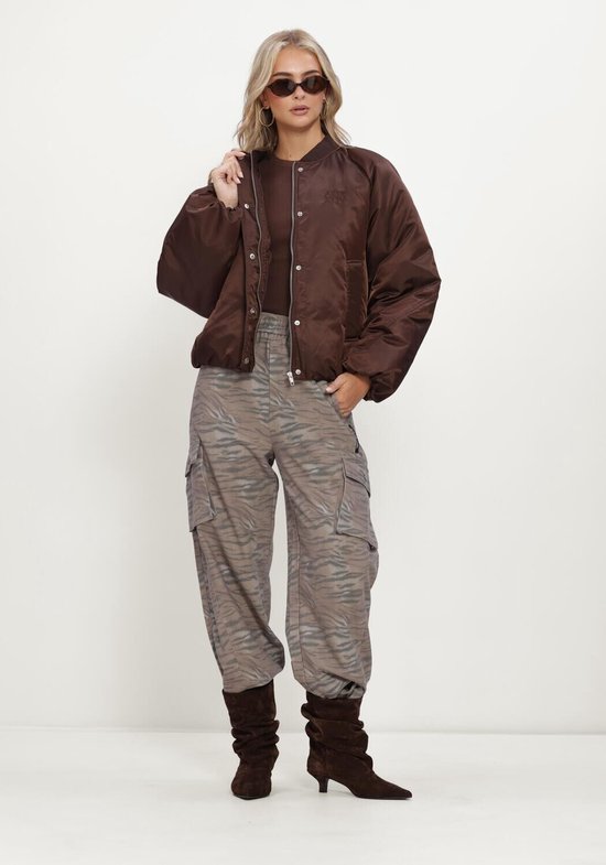 Model draagt een bruine bomberjack met rits en de ALX geborduurde logo, gecombineerd met een bruin shirt en dierenprint broek.