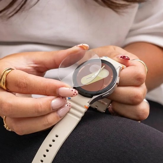 Persoon plaatst een ronde, transparante Strap-it screenprotector van gehard glas op een beige Samsung Galaxy Watch.