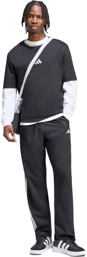 Man met zwarte Adidas sportbroek met witte strepen, zwart T-shirt met lange mouwen en een schoudertas.
