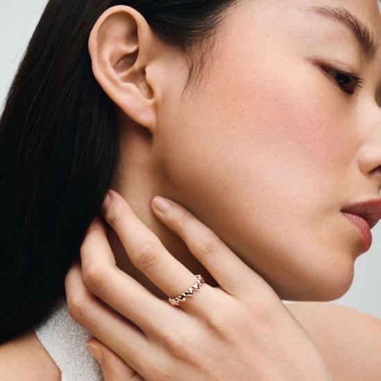 Model draagt een roze gouden ring met hartjes aan haar hand.