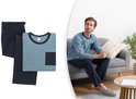 Man op bank in lichtblauw pyjamapak met donkerblauwe broek en zak. Naast pyjamaset.