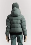 Meisje draagt van achteren gezien een donkergroene, gewatteerde winterjas met capuchon. Ze draagt een groene muts.
