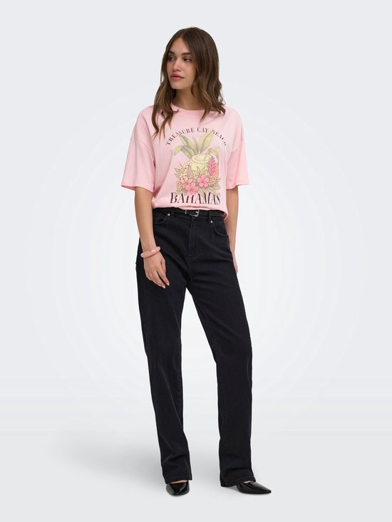 Model in roze T-shirt met 'Bahamas' opdruk en zwarte jeans, staand op een witte achtergrond.