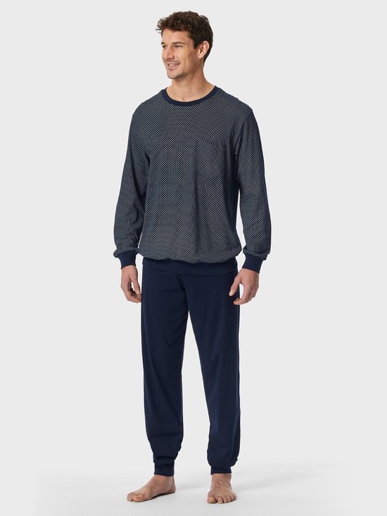 Model draagt een marineblauwe pyjama met een wit stippenpatroon op de top en een effen broek met boorden.