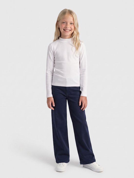 Blond meisje draagt een wit geribbelde coltrui met lange mouwen en donkerblauwe wide-leg jeans met witte sneakers.