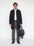 Man met witte hemd, grijze wijde broek, zwarte riem, zwart jasje en zwarte weekendtas.