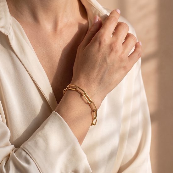 Close-up van een hand met een goudkleurige schakelarmband in een zijden blouse.