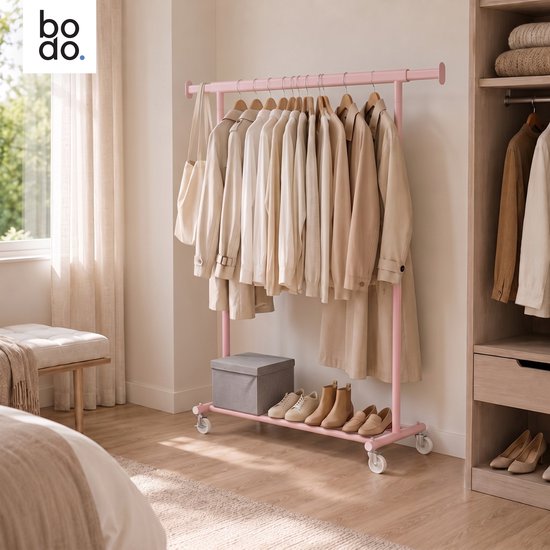 Roze kledingrek in een slaapkamer met beige kleding, een tas, een grijze doos en schoenen op de onderste plank.