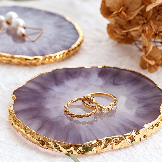 Twee paarse schaaltjes met gouden randen op een lichte ondergrond, een met ringen en een met oorbellen.