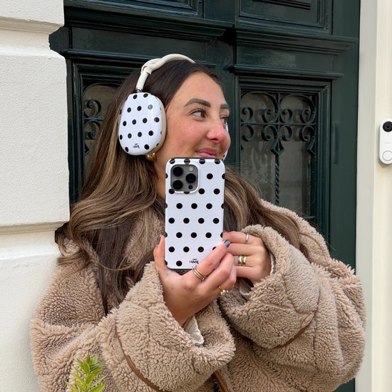 Vrouw met witte koptelefoon en witte telefoonhoes met zwarte stippen.