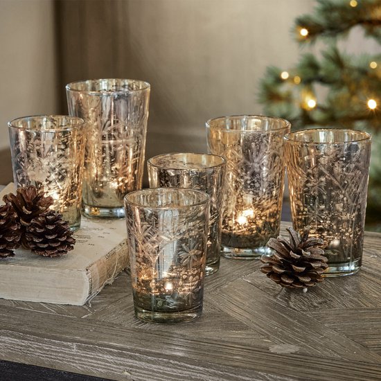 Set van zes antiekzilveren glazen windlichten met sneeuwvlokmotief op een houten tafel met dennenappels.