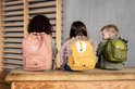 Drie kinderen op een bankje met rugzakken in de vorm van Mrs. Cat (roze), een leeuw (geel) en een dino (groen).