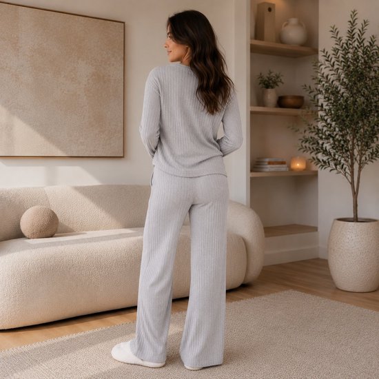 Model van achteren gezien in een lichtgrijze geribbelde lounge-set met wijde broek en witte pantoffels.