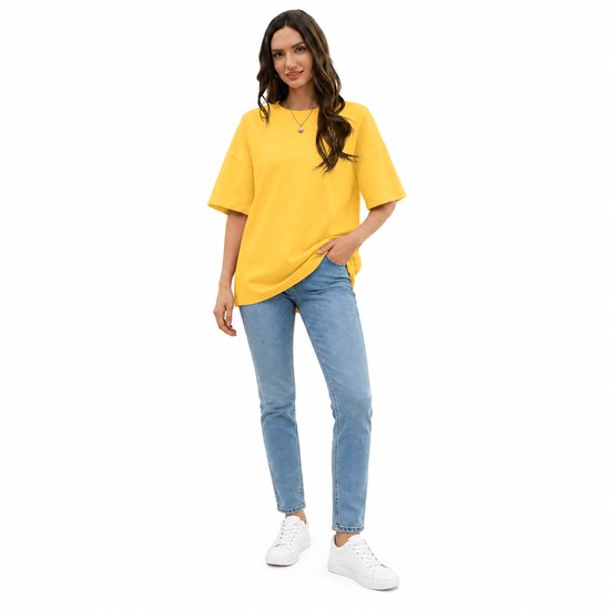 Model in oversized geel T-shirt met ronde hals, gecombineerd met een blauwe jeans.