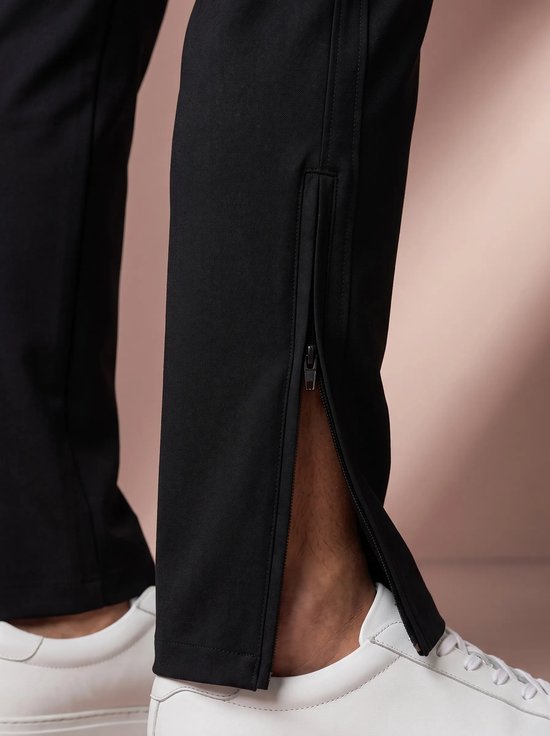 Zwarte sportbroek met rits aan de zijkant van de broekspijp, gedragen met witte sneakers.
