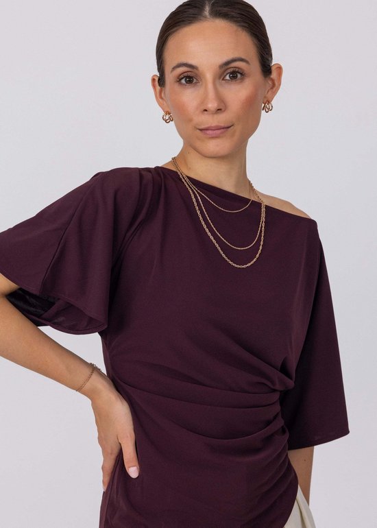 Model draagt gouden Purelei ketting met meerdere schakels en een subtiele armband. Haar paarse top is off-shoulder.