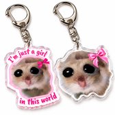 Twee acryl sleutelhangers met een hamster, roze strik en tekst “I’m just a girl in this world”.