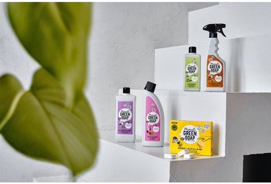 Assortiment Marcel's Green Soap schoonmaakmiddelen op witte treden, met deels onscherp groen blad op de voorgrond.