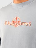 Close-up van een lichtblauwe sweater met het Brunotti logo en een gestileerd kompas in oranje tinten.