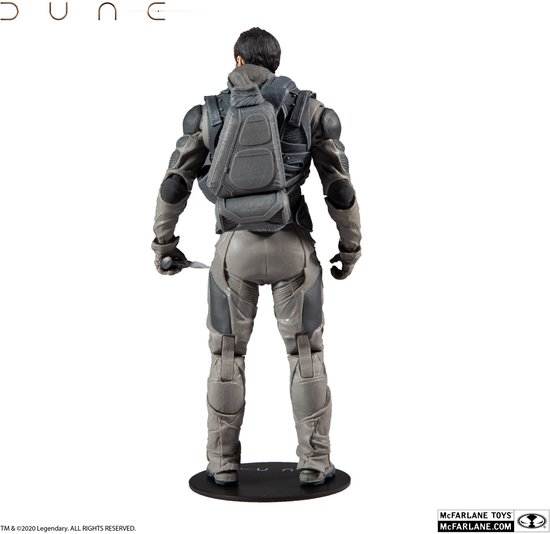 Dune actiefiguur van achteren bekeken, met een grijs harnas, rugzak en een mes in de hand, op een zwarte standaard.
