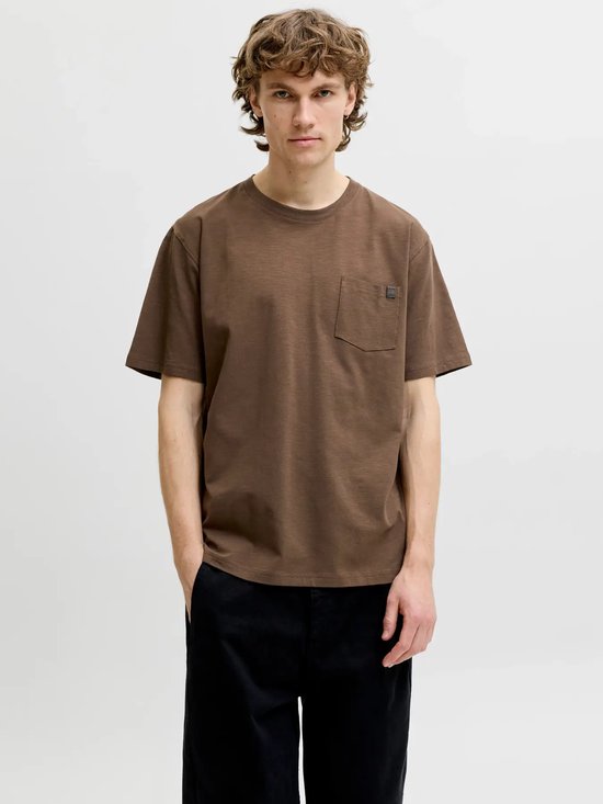 Model draagt een bruin t-shirt met borstzak en zwarte broek.