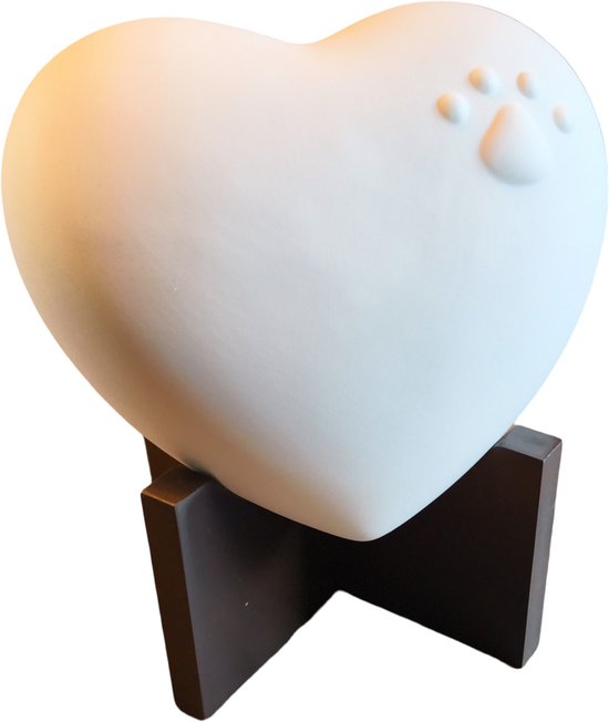 Wit hartvormig urn met dierenpootje op een donkerbruine houten standaard.