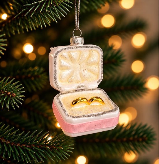Kersthanger in de vorm van een open roze sieradendoosje met twee gouden trouwringen, hangend in een kerstboom.