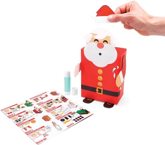 Een hand plaatst een kerstmuts op een cadeau, versierd als een kerstman met gouden knopen.