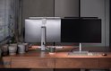 Twee computers met zilverwitte BenQ monitorlampen op een houten bureau, één lamp aan het werk.