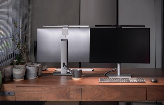 Twee computers met zilverwitte BenQ monitorlampen op een houten bureau, één lamp aan het werk.