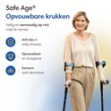 Een oudere vrouw met een beige trui en broek, staand met krukken. De krukken zijn zwart met blauwe handvatten en manchet.