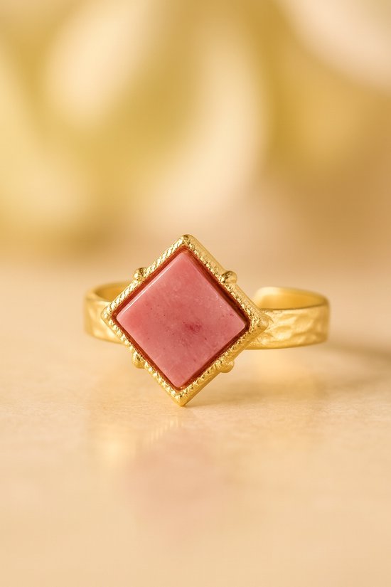 Gouden ring met een roze, ruitvormige steen en een gekartelde rand, op een hamerslag band.