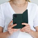 Vrouw met gouden ketting houdt open groene leren Selencia bookcase met telefoon vast.
