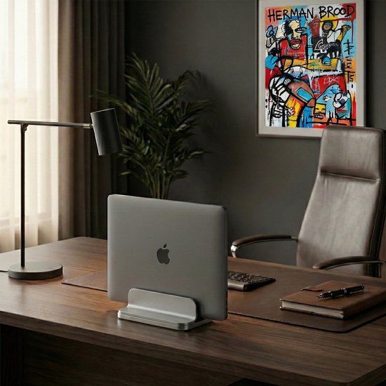 MacBook op een grijze, verstelbare laptopstandaard op een bureau, met schilderij en stoel.