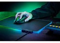 Een hand gebruikt een zwarte Razer gaming muis met groene details, geplaatst op een zwart gamingmuismat met gloeiende groene en blauwe randen.