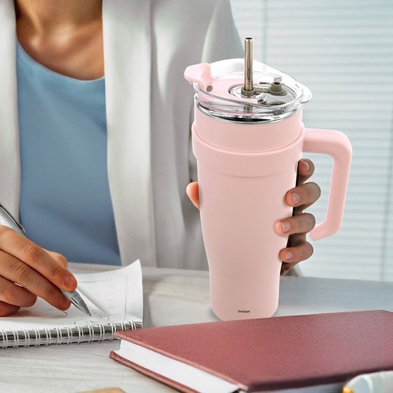Roze thermosbeker met een lichtroze handvat en deksel, vastgehouden door een persoon aan een bureau.