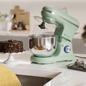 Pastelgroene keukenmachine naast een chocoladetaart op een marmeren aanrecht.