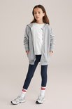 Meisje in donkerblauwe legging, wit t-shirt en grijze hoodie, staand.