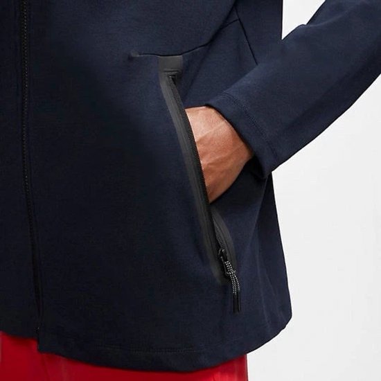 Man met donkerblauwe Nike Tech vest met rits, met hand in de zak.