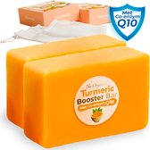 Twee oranje blokken kurkumazeep op de voorgrond. Op de achtergrond twee verpakkingen, een netje en een schild met "Met Co-enzym Q10".