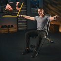 Man in grijs shirt traint met een zwarte fitnessbank en weerstandsbanden, met detailafbeelding van de bandbevestiging.
