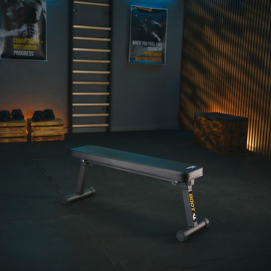 Een lege zwarte trainingsbank met 'TX 100B' op de zijkant, in een fitnessruimte.