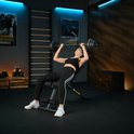 Vrouw met zwarte sportkleding ligt op een zwarte fitnessbank en tilt een halterstang omhoog.