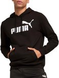 Man draagt een zwarte PUMA hoodie met wit logo en steekt handen in de zakken.