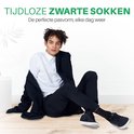 Man zittend met een zwarte blazer, wit overhemd en zwarte sokken.