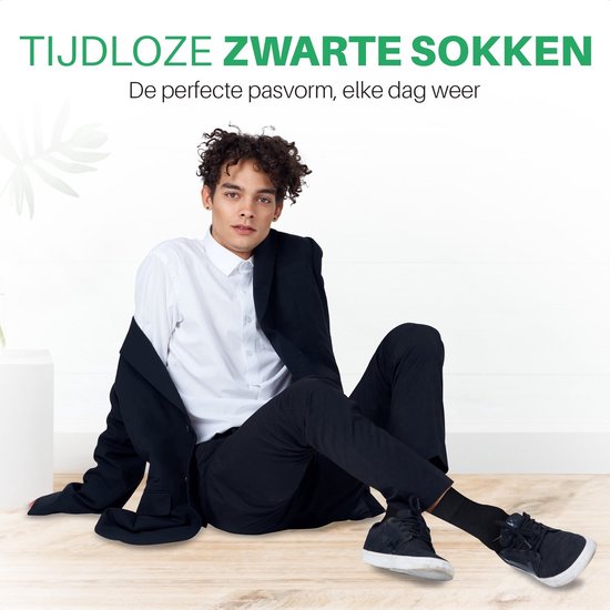 Man zittend met een zwarte blazer, wit overhemd en zwarte sokken.