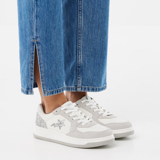 Voeten van een vrouw in blauwe jeans en witte sneakers met grijze suède en glitter.