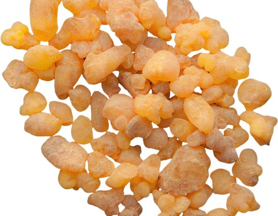 Een hoopje gele tot oranje wierookharsstukjes op een witte achtergrond.