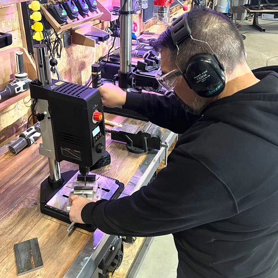 Man in gehoorbescherming die een boormachine bedient in een werkplaats.