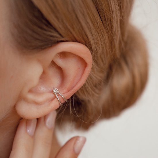 Vrouw draagt een zilveren oorklem met twee ringen en een kleine zirkonia op haar oor.